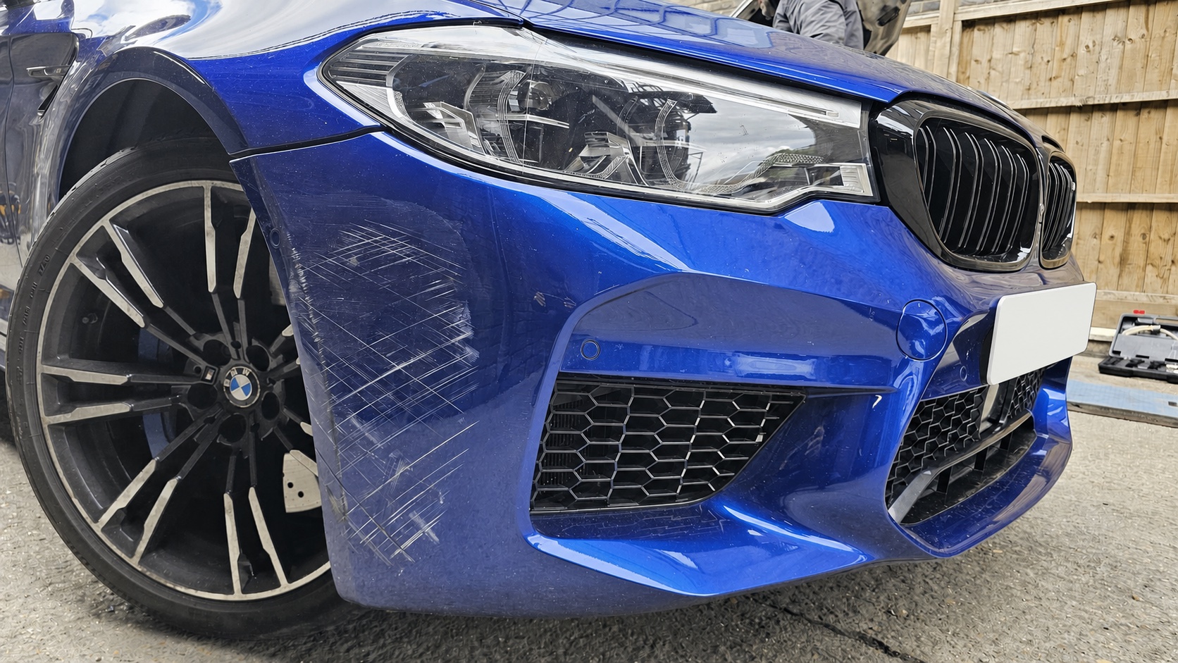 Blue BMW M5 with visible front bumper scratches before repair
